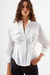 Camisa azul de algodón con finas rayas blancas verticales, cuello mao, manga larga y detalle de pinzas y botones en la zona de la cintura. Posee dos bolsillos de parche con tapa en el pecho.