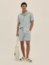 Conjunto de camisa de manga corta con cuello solapa y short con cordón ajustable, ambos en tejido ligero a rayas verticales celestes y blancas.