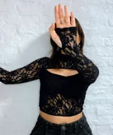 Top de encaje negro con diseño tipo corset, cuello alto y mangas largas con guantes integrados. Presenta una abertura frontal en el pecho y el área del busto forrada.