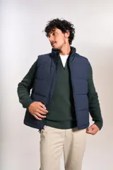 Chaleco puffer de color azul marino, con cierre frontal completo y cuello alto. Presenta un diseño acolchado horizontal y el logo de la marca bordado en el pecho.