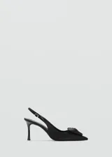 Zapato de tacón destalonado color negro de tejido satinado, con punta fina, cierre de hebilla ajustable en la tira del talón, tacón de aguja y detalle de flor decorativa en el empeine.