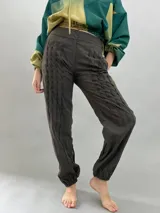 Pantalón tipo babucha confeccionado en lana de oveja, color visón. Presenta un diseño de tiro alto con textura vertical plisada a lo largo de las piernas, cintura con cierre de doble broche y puños elásticos en los tobillos.