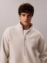 Buzo polar de Calvin Klein en color beige, con cuello alto tipo mock neck y cierre de media cremallera frontal. Presenta un diseño de corte regular con mangas largas, bajo ajustable con cordón y logo de la marca bordado en el pecho.