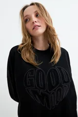 Buzo negro con efecto lavado, cuello redondo y manga larga. Presenta un diseño estampado en relieve con forma de corazón y la inscripción "Good Mood" en el centro.