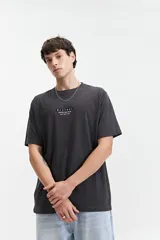 Remera de manga corta color gris oscuro, con escote redondo y ajuste regular. Presenta un estampado frontal con el texto "MISTRAL KAMIOKA NEW TRIAL SINCE 1976 // NLD".