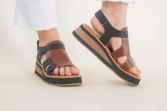 Sandalias de cuero color marrón con plataforma de madera y suela de goma negra. Tiras anchas de cuero marrón en el empeine y tobillo con ajuste de hebilla.