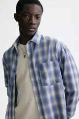 Camisa de manga larga con ajuste relajado, cuello inglés y un bolsillo aplicado en el pecho. Presenta cierre frontal de botones y bajo redondeado.