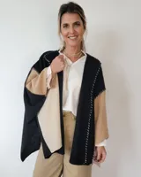 Ruana de lana color negro, beige y tostado, con diseño geométrico y flecos en el borde inferior.