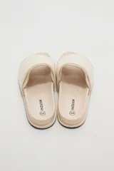 Sandalias planas color marfil, con tira ancha acolchada en el empeine y suela baja con borde oscuro.