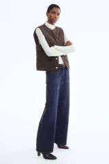 Chaleco guateado color marrón oscuro, con cuello redondo, cierre frontal con botones a presión dorados y dos bolsillos de parche en la parte delantera.