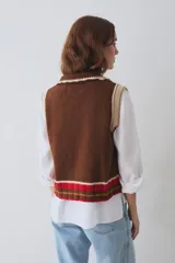 Chaleco de lana tejido con cuello bebé festoneado, cierre frontal de botones, bolsillo decorativo y detalles de rayas en contraste en los bordes y el ruedo.