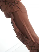Pantalón de lino color beige, con apliques de tela con volados y costuras decorativas que aportan textura y movimiento. Cuenta con diseño de pernera ancha, bolsillos y aberturas laterales.