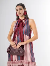 Vestido largo de corte halter en organdí, con estampado de rayas verticales y horizontales en tonos bordó, azul y crudo. Cuenta con un lazo en el cuello y un volado en la parte inferior.