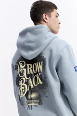 Canguro con capucha de algodón color celeste, con estampa gráfica en la espalda que incluye flores y la frase 'Grow Back'. Presenta un parche pequeño en la manga y corte regular.