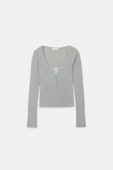 Chaqueta de punto color beige con escote en pico y manga larga, que incluye un top interior integrado con detalle de encaje a tono. Cierre frontal mediante botones.