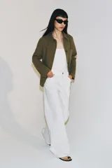 Chaqueta de estilo utilitario color verde militar, con cuello solapa, manga larga y cierre frontal con botones ocultos por solapa. Presenta bolsillos con solapa en la parte delantera y un bolsillo de plastrón en el pecho.