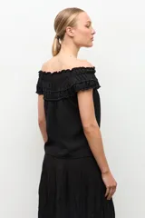 Blusa negra estilo bardot con escote de hombros descubiertos, detalles de volados fruncidos en el pecho y diseño sin mangas.