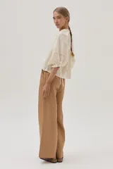 Blusa color crudo con bordado calado, cuello con volantes y lazos para ajustar. Mangas abullonadas con puños elásticos y lazos.