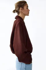 Campera oversized de sarga color marrón, con cuello, cierre frontal y bolsillos laterales ribeteados. Cuenta con mangas abullonadas, puños elásticos y bajo globo para una silueta redondeada.