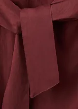 Vestido midi color bordó con cuello redondo, sin mangas y corte recto, con detalle de nudo y lazo ajustable en la cintura.