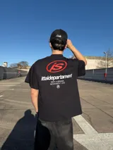 Remera negra de manga corta y corte oversize, con estampa en la espalda que incluye el logo 'IS' en rojo y texto blanco con la leyenda 'ittaidepartament NOT A BRAND, MOVEMENT 04D'.