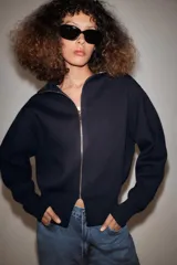 Chaqueta de punto color azul marino, de cuello alto y manga larga, con cierre frontal de cremallera metálica y detalle de abertura en el bajo delantero.
