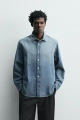 Camisa de corte relajado confeccionada en denim de algodón con efecto lavado. Presenta cuello solapa, cierre frontal de botones y mangas largas con puños abotonados.