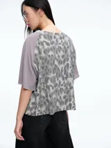 Remera de corte boxy con estampado animal print en el frente y mangas raglán en color gris liso. Presenta un bolsillo frontal y mangas 3/4 con terminación sin costura.