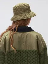 Campera tejido grueso y abrigado color verde militar, con forro de nylon interno, cuello estilo camisa en color negro y cierre frontal con botones. Cuenta con cuatro bolsillos delanteros con apliques en distintos tonos y texturas, y un parche bordado circular en el bolsillo superior izquierdo.