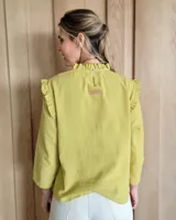 Blusa blanca de manga larga con cuello alto y volados en cuello y hombros.