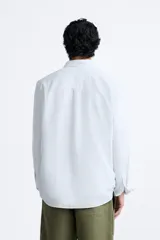 Camisa celeste a rayas verticales, de corte relaxed fit, confeccionada en lino y algodón. Tiene cuello abotonado, manga larga con puños abotonados, bolsillo de parche en el pecho y cierre frontal con botones.