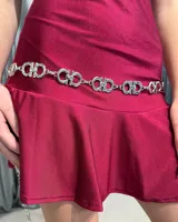 Cinturón de cadena metálica plateada compuesto por eslabones circulares entrelazados con diseño geométrico central.