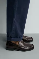 Mocasín de vestir color marrón oscuro, fabricado en cuero, con detalle de antifaz en el empeine y suela a tono con ligero tacón.