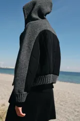 Chaqueta de punto con capucha, manga larga y cierre frontal con cremallera metálica. Presenta un diseño de tejido texturizado en color gris oscuro con detalles en contraste en los puños.