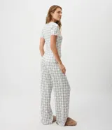 Pijama largo de dos piezas confeccionado en tejido peach touch, con estampado de cuadros y pequeños detalles florales. Incluye una blusa de manga corta con escote en V, frunce en el busto y bordes ondulados, y un pantalón de corte recto con cintura elástica y cordón ajustable.