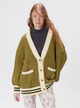 Cardigan de tejido de punto grueso en color verde oliva, con diseño oversize. Presenta cuello en V, cierre frontal con botones, dos bolsillos delanteros y terminaciones acanaladas en puños y ruedo con detalles en color crema y verde oscuro.