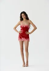 Vestido corto de lentejuelas rojas con detalles de encaje rosado en el escote y el ruedo, de corte recto y tirantes finos.
