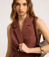 Chaleco marrón de corte sastre con cuello blazer, doble botonadura dorada y bolsillos simulados. Fabricado con procesos más sustentables.