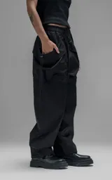 Pantalón de estilo utilitario y corte oversize, confeccionado en textil técnico liviano. Presenta cintura elástica con cordón ajustable, bolsillos laterales envolventes de gran tamaño con cordones y tancas de ajuste, y elásticos regulables en los tobillos.