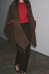 Capa de punto color marrón, con escote en V, mangas cortas y bolsillos de plastrón en el delantero. El ruedo tiene un corte asimétrico.