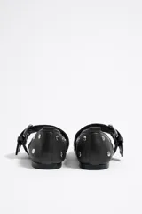 Bailarinas negras de cuero con punta fina, tachas plateadas y correa con hebilla metálica. Zapato plano con suela fina.