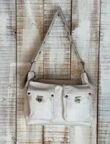 Bolso de hombro color beige con textura de cuero grabado tipo cocodrilo. Presenta dos bolsillos frontales con solapa y cierres metálicos, y una correa ancha ajustable con ojales metálicos.