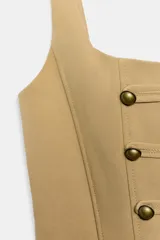 Top corsetero de color tostado con escote cuadrado, tirantes anchos y cierre de cremallera en la espalda. Cuenta con costuras marcadas y filas de botones metálicos dorados decorativos en el frente.