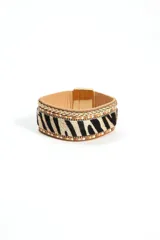 Brazalete ancho con base de cuero color beige, estampado de cebra en blanco y negro, bordes con cuentas doradas y cierre magnético dorado.