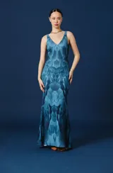 Vestido largo sin mangas de color azul, con escote en V y un estampado simétrico que simula plumas en tonos celestes y azules oscuros. Tiene una silueta fluida y entallada.
