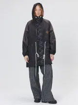 Campera tipo piloto con capucha, cierre frontal con botones y detalle de costuras en zigzag. Presenta cordones ajustables en la cintura y capucha, puños elásticos y logo bordado en el pecho.