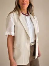 Chaleco sastrero color beige con solapas clásicas, bolsillos con solapa y cierre frontal con un botón.