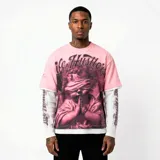 Remera rosa de corte oversize con diseño de doble capa, que incluye mangas largas blancas integradas. Presenta un estampado gráfico frontal de un querubín con los ojos vendados y texto decorativo. Posee detalles de efecto desgastado en el cuello y las mangas.