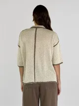 Chaqueta de punto calado en color negro con detalles de bordes en color crudo. Presenta cuello camisero, cierre frontal con botones, mangas cortas y un bolsillo frontal tipo parche.