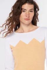 Buzo de tejido de punto con diseño bicolor, combinando blanco en la parte superior y mangas con un tono celeste grisáceo en el cuerpo, presentando un patrón geométrico en la unión de los colores. Posee cuello redondo y mangas largas.